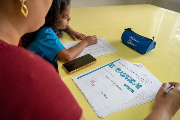 Foto de professora e estudante - avaliação de fluência de leitura - redes municipais