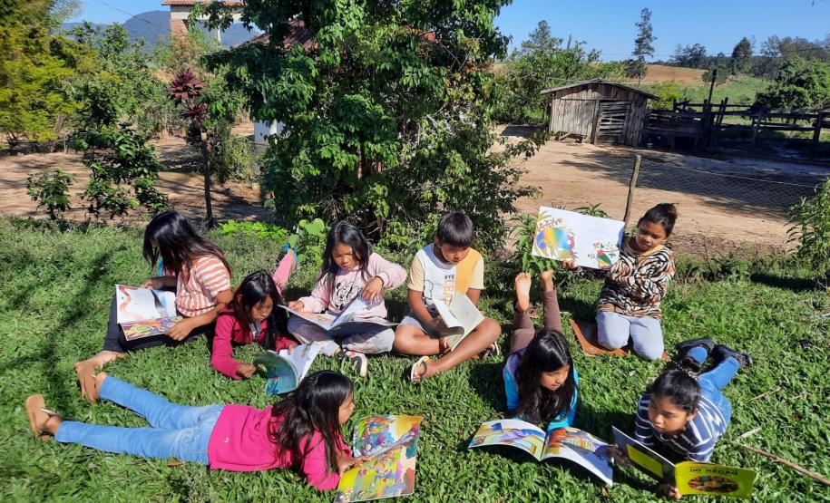 Foto de um grupo de estudantes indígenas lendo embaixo da árvore