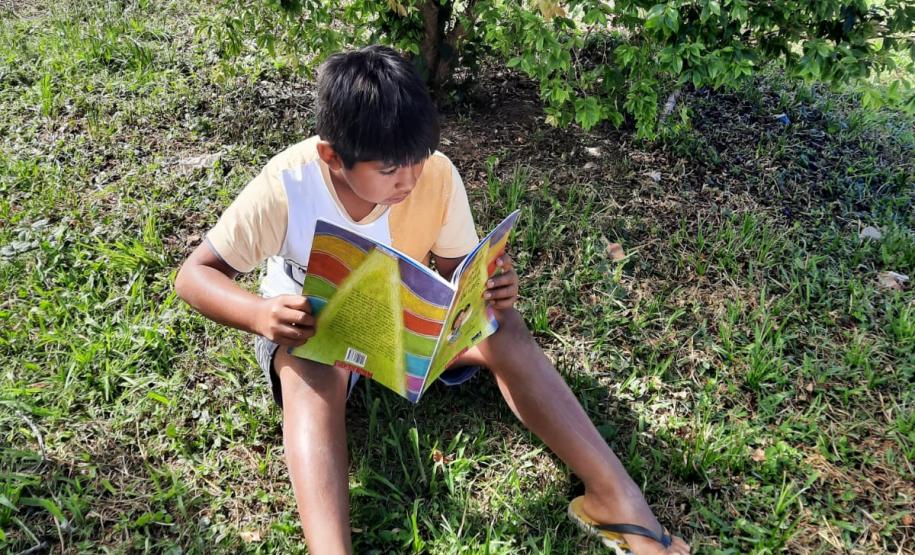 Foto de um estudante indígena lendo embaixo da árvore