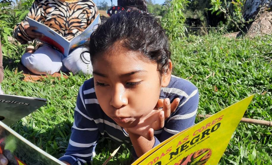 Foto de duas estudantes indígenas lendo sob o sol