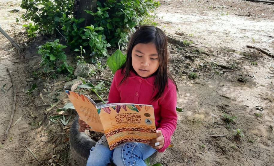 Foto de uma estudante indígena lendo embaixo da árvore
